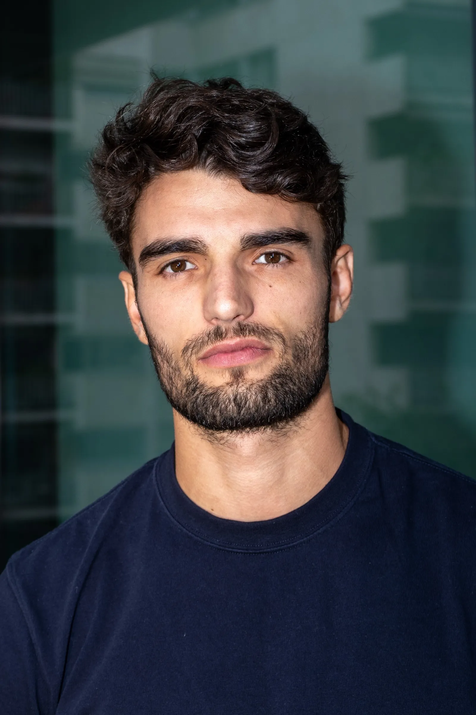 Portrait of a man with dark curly hair in a navy T-shirt