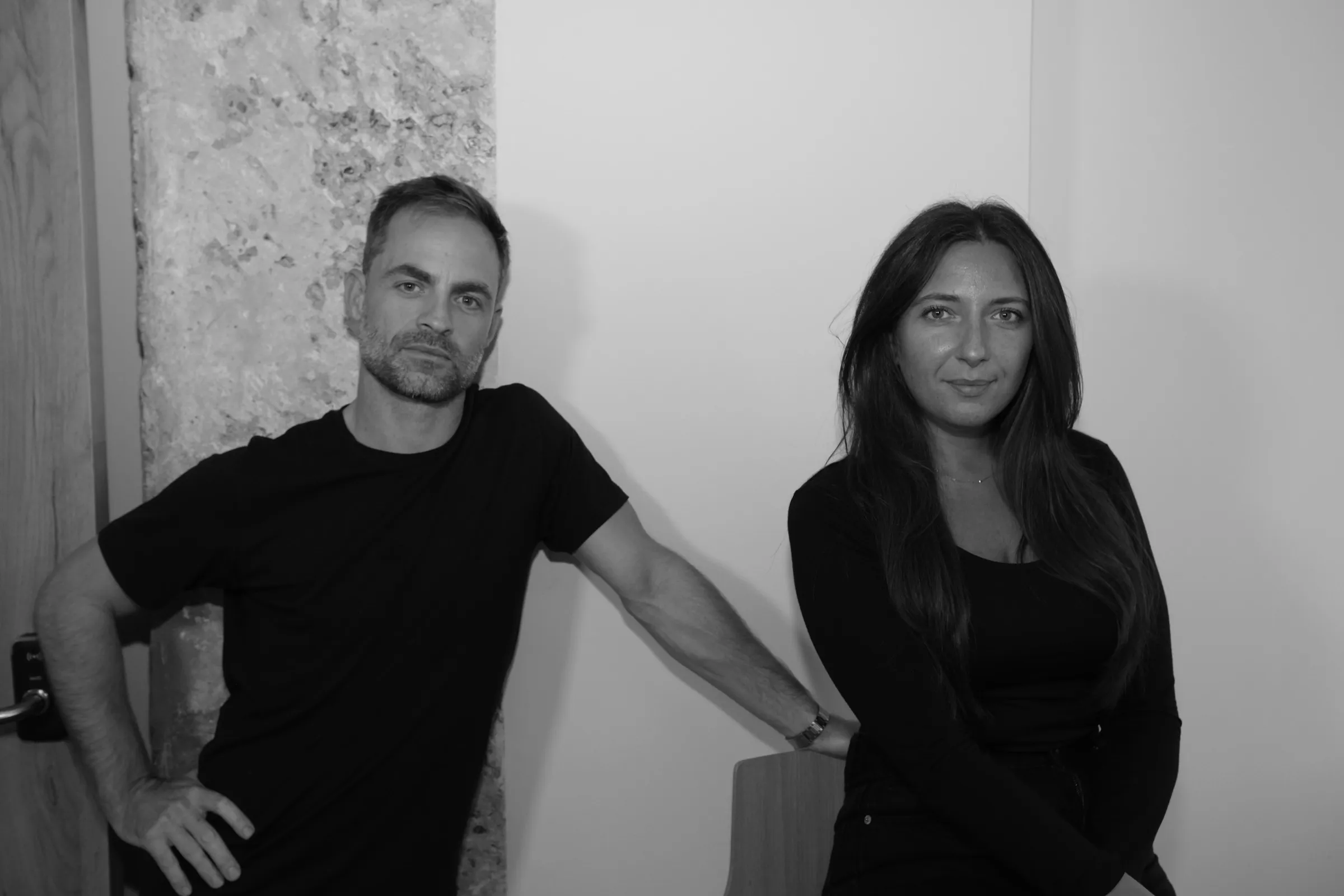 Black and white portrait of a man and a woman dressed in black against a white wall